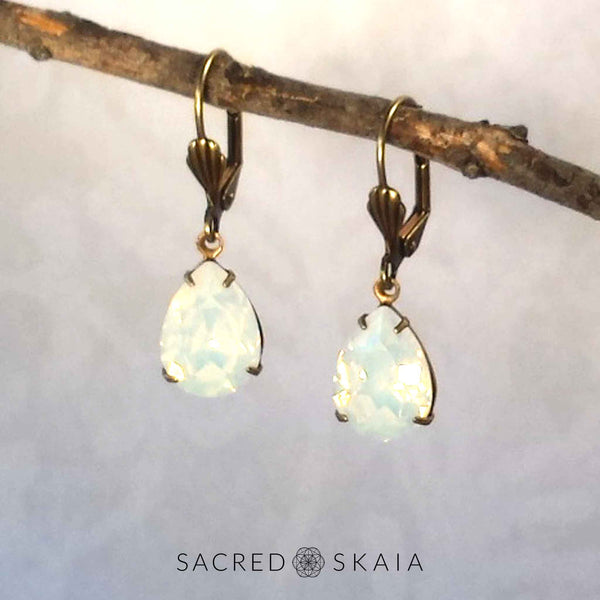 Vintage-style Aphrodite Crystal Teardrop Earrings with oxidized brass settings, lever back ear wires and pear-shaped white opal Swarovski crystals, shown hanging on a branch