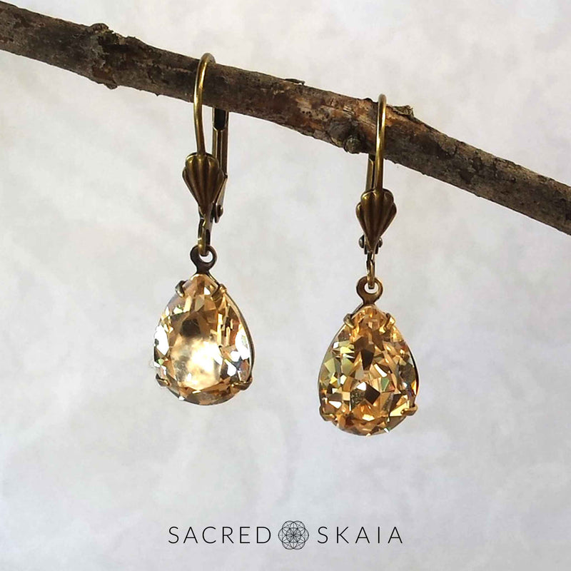 Aphrodite Crystal Teardrop Earrings with oxidized brass settings, lever back ear wires and pear-shaped light silk (pale gold) Swarovski crystals, shown hanging on a branch as an alternate color choice